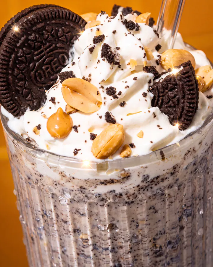 Macro view of a cookies-and-cream shake topped with whipped cream, cookies and peanuts.